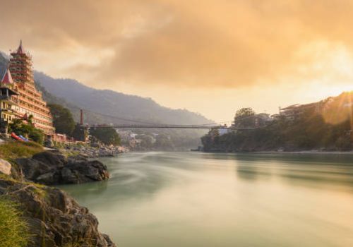 Stunning view of the Ganga river embankment with the Lakshman Jhula bridge and Tera Manzil Temple (Trimbakeshwar) during a beautiful sunset. Rishikesh, Uttarakhand, India.